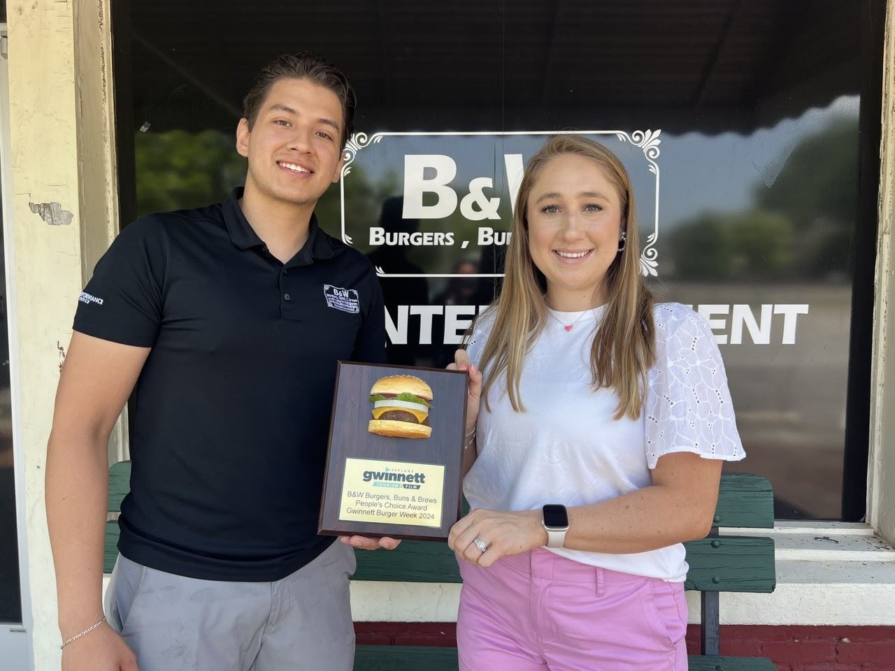B&W owner poses with Explore Gwinnett in front of restaurant holding Burger Week Plaque
